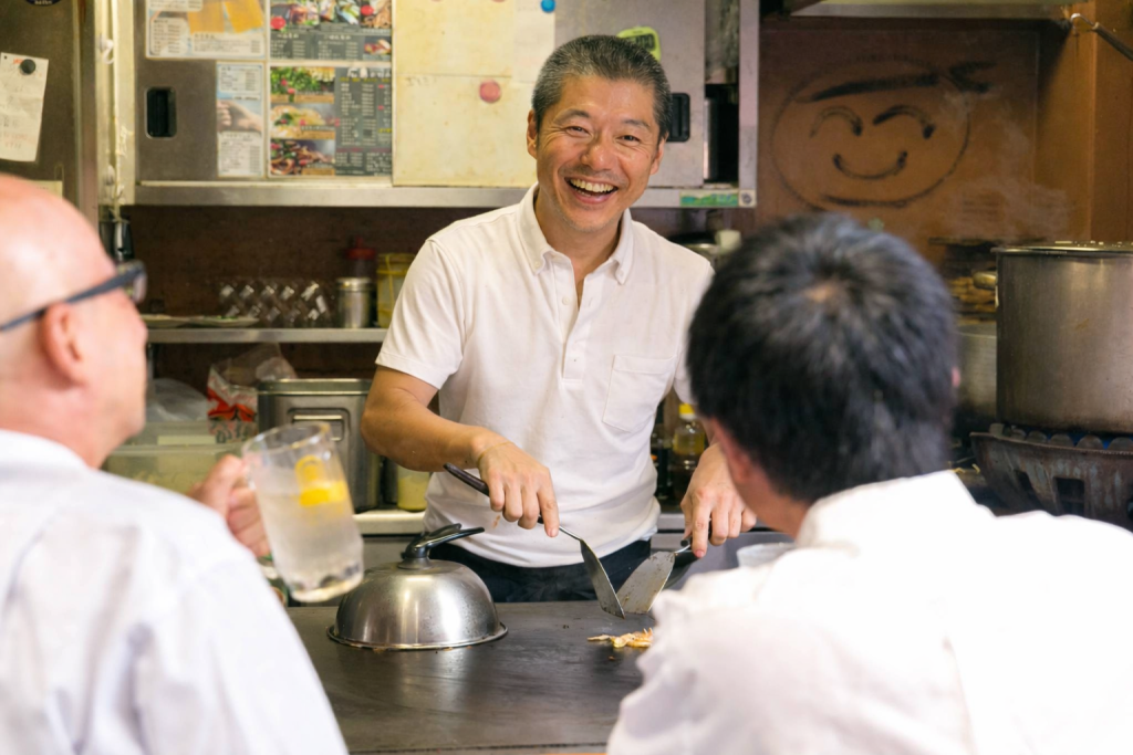 鉄板の前で、お客様と楽しく会話しながら広島お好み焼きを焼く、弘々家店長市山